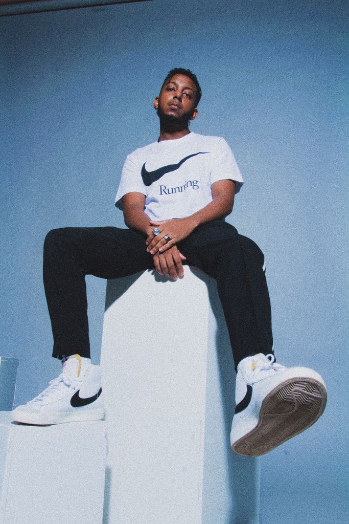 Low-angle portrait of a man sitting casually in Nike attire. Urban and youthful vibe captured indoors.